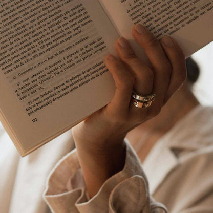 Hand holding a book, adorned with AN JEWELS JEWELRY Mod. AL.RWH01SC-9 rings, showcasing elegant design and craftsmanship.
