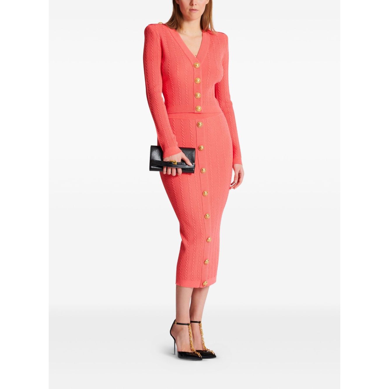 Woman wearing Balmain Long-sleeved twisted knit cardigan in coral pink, with logo-embossed buttons and epaulettes.