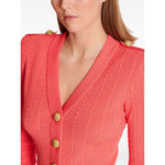 Balmain Long-sleeved twisted knit cardigan in coral pink with logo-embossed buttons and epaulettes, showing a close-up of the V-neck style.