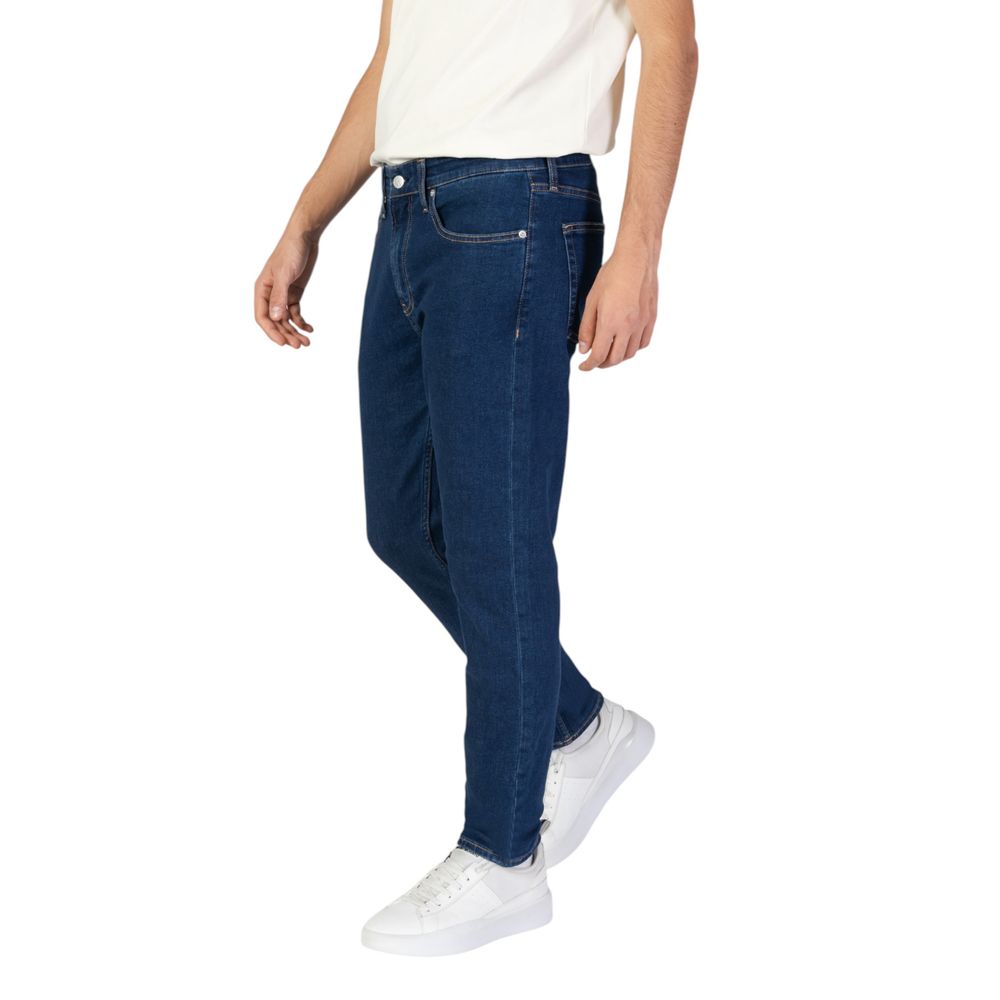 Man wearing Calvin Klein Jeans Blue Cotton Slim Fit Jeans with white sneakers, showcasing tapered leg design and modern style.