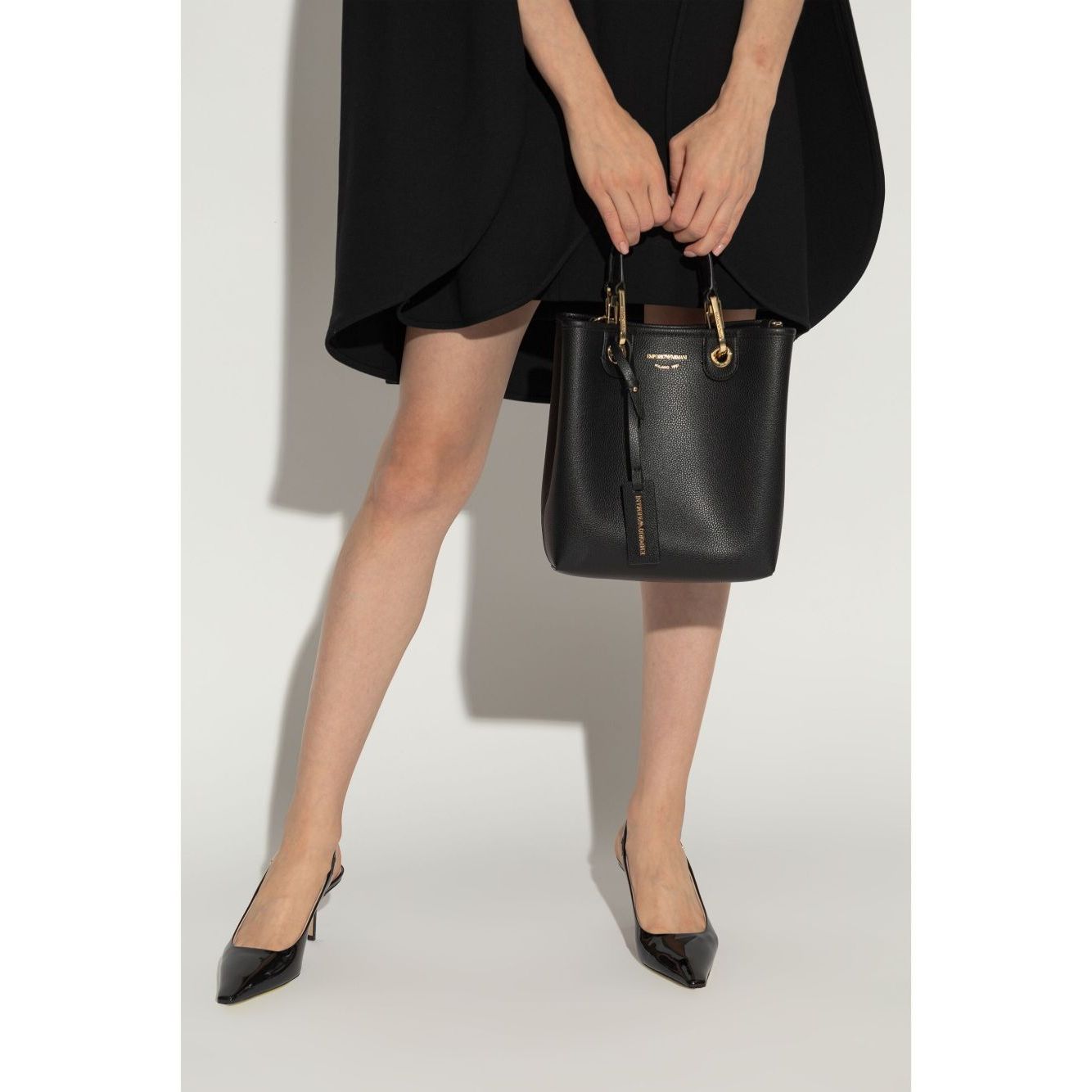 Emporio Armani MyEA shopping bag in black with logo print and shoulder strap, paired with a black dress and heels, front view.
