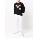 Emporio Armani Sweaters Black cotton modal crewneck with chest logo, long sleeves, and straight hem, styled with white pants and sneakers.