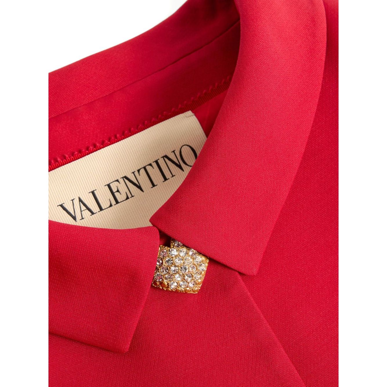 Close-up of Valentino Crepe Couture Jacket with red fabric and pointed collar. Featuring Valentino label and button detail. Luxury fashion.
