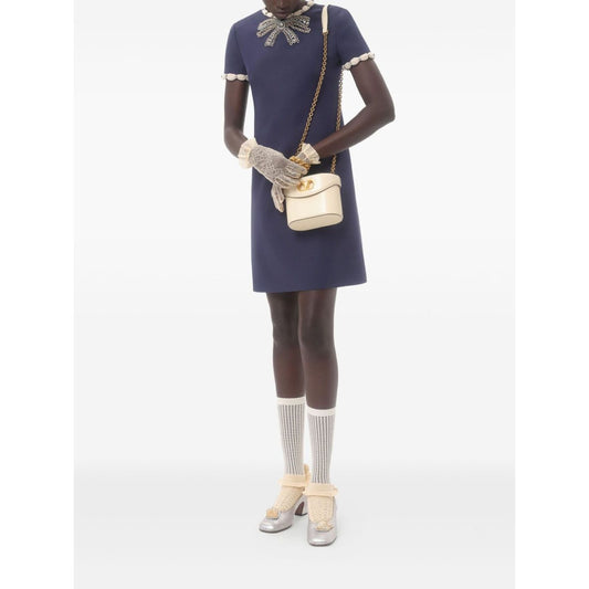 Model wearing Valentino Short Embroidered Crepe Couture Dress with rhinestone embellishments and contrasting trim, holding a cream bag.