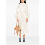 Woman wearing Zimmermann Shirts Ivory, embroidered blouse, with long sleeves, cut-out floral details and elastic cuffs, holding a tan bag.